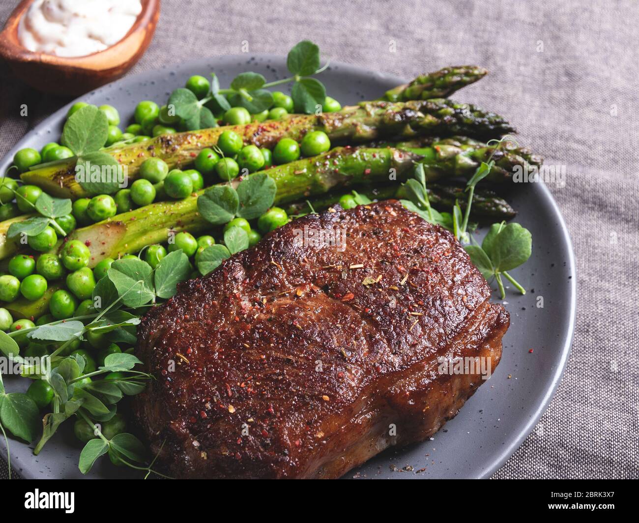 bistecca di manzo arrosto, montone con piselli verdi di asparagi su un piatto, salsa bianca Foto Stock