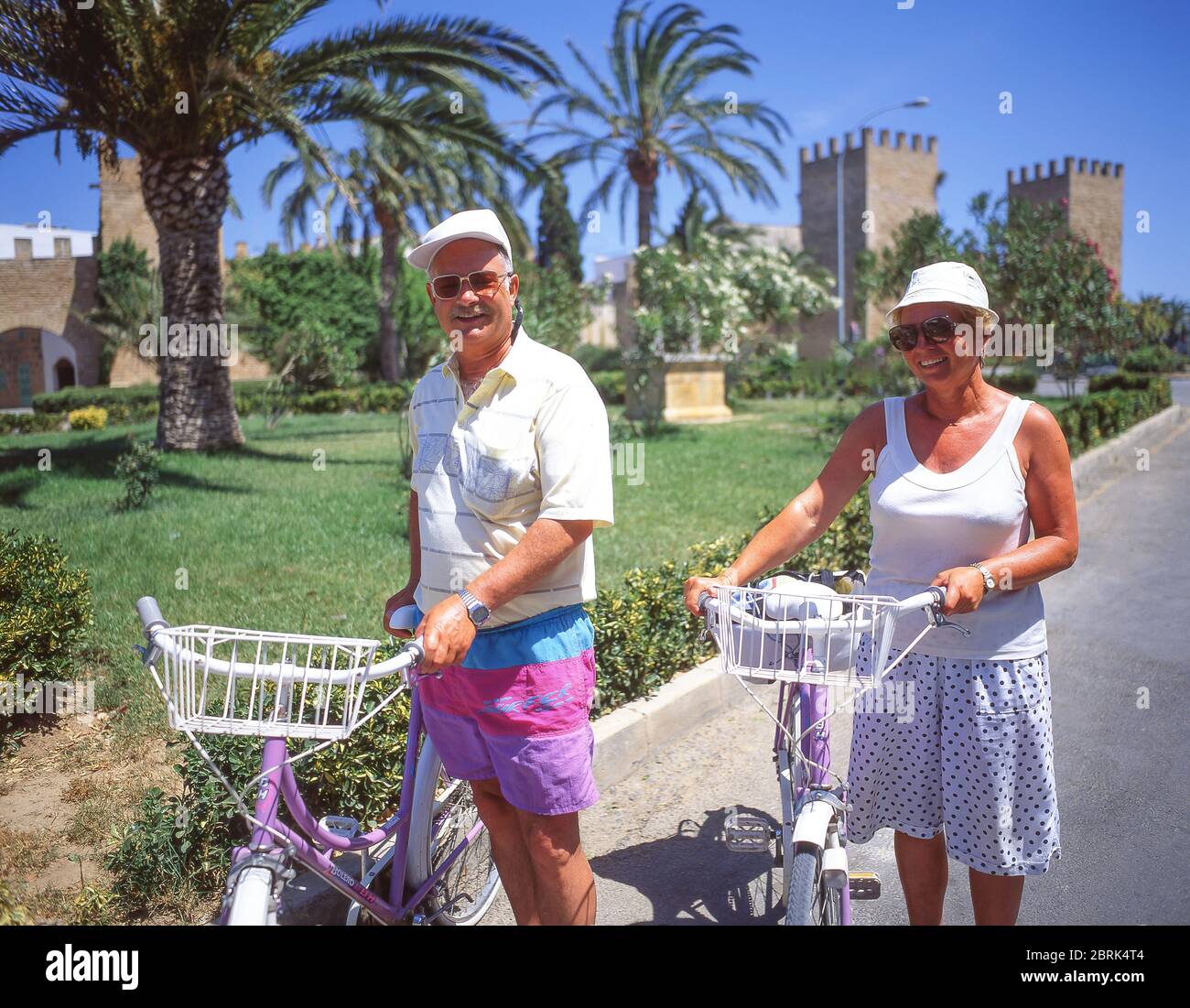 Coppia di anziani con le biciclette al di fuori alle mura della vecchia città, Alcudia, Alcudia comune, Maiorca (Mallorca), isole Baleari, Spagna Foto Stock