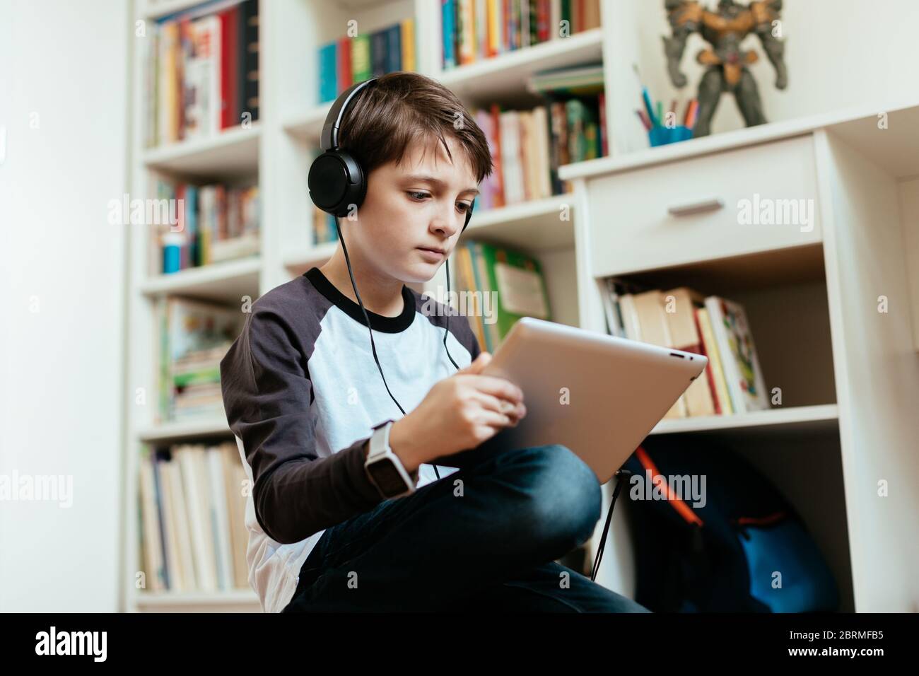 Ragazzo che fa i suoi compiti su un tablet digitale a casa. Giovane studente che lavora per conto proprio sulle assegnazioni scolastiche. Foto Stock