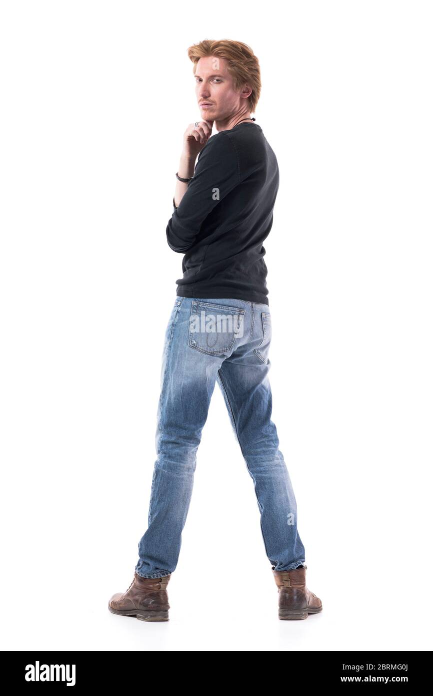 Vista posteriore di un giovane sicuro che gira e guarda la fotocamera con la mano sul mento. Lunghezza corpo intero isolata su sfondo bianco. Foto Stock
