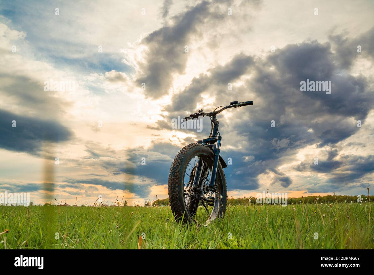 Una bicicletta con ruote spesse su un prato verde contro un cielo bellissimo. Moto da fatbike. Foto Stock