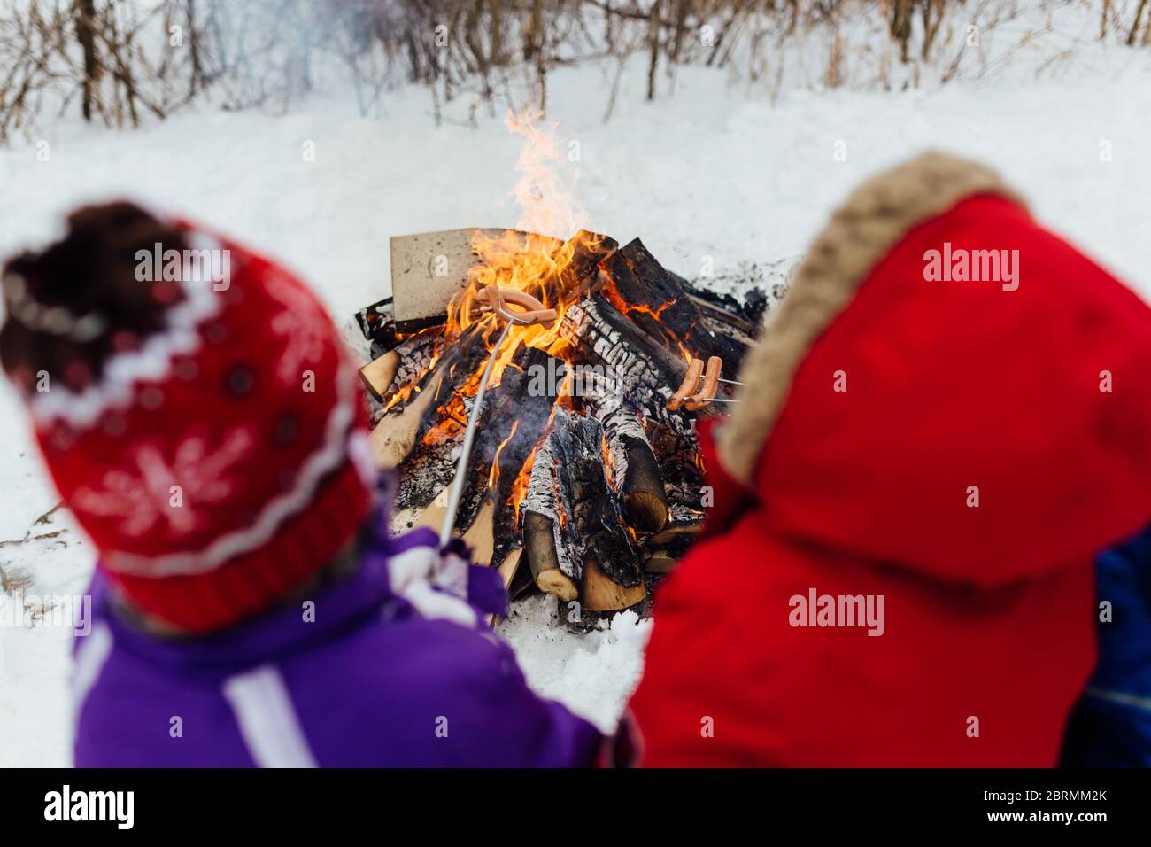 2 bambini in campeggio in inverno tostando hot dog sopra il fuoco Foto Stock