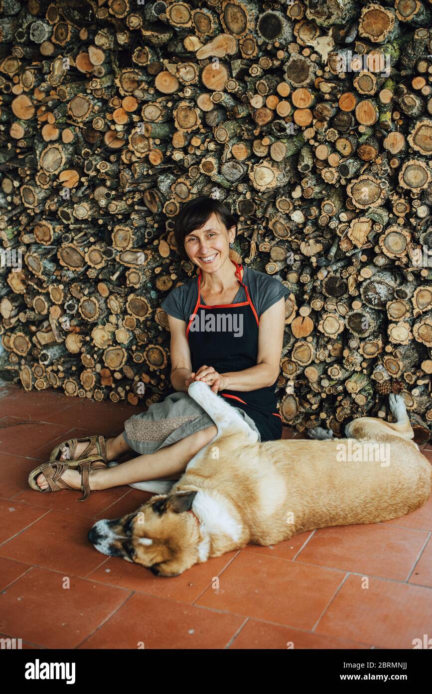 Donna sorridente che gioca con il cane al mucchio di tronchi a. Villaggio in Portogallo Foto Stock