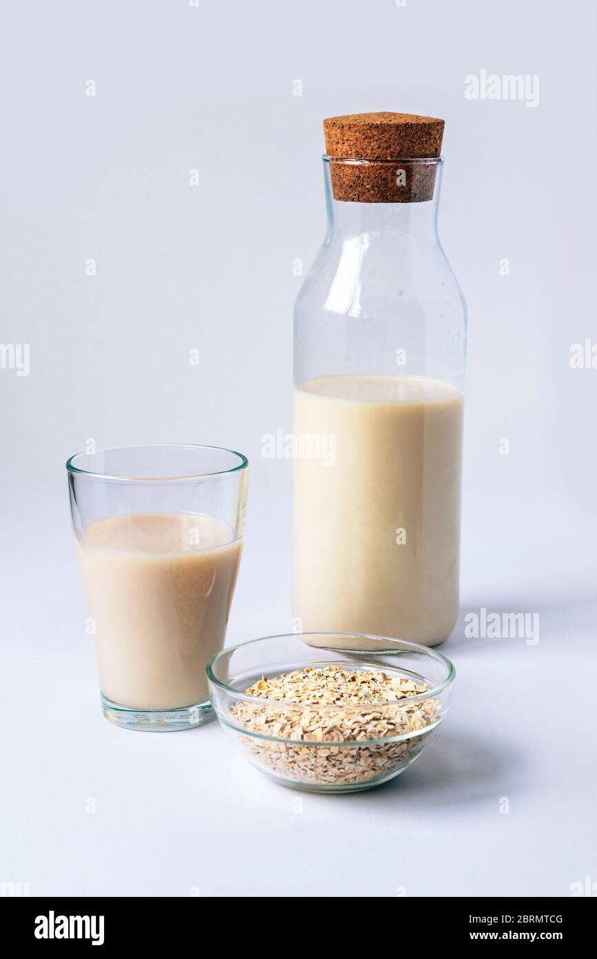 Un bicchiere e una bottiglia di latte di avena non caseario su tavola bianca. Concetto di cibo sano. Foto Stock