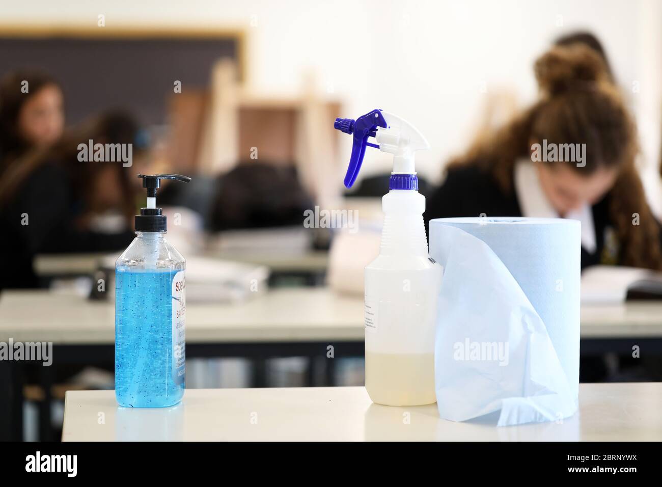 Deliberatamente offuscato gli studenti in background che lavoravano sulle classi. Pompa igienizzante per mani con flacone spray disinfettante in primo piano. Foto Stock