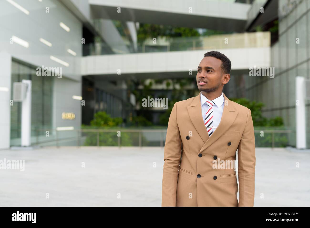 Felice giovane bell'uomo d'affari africano che pensa in città Foto Stock