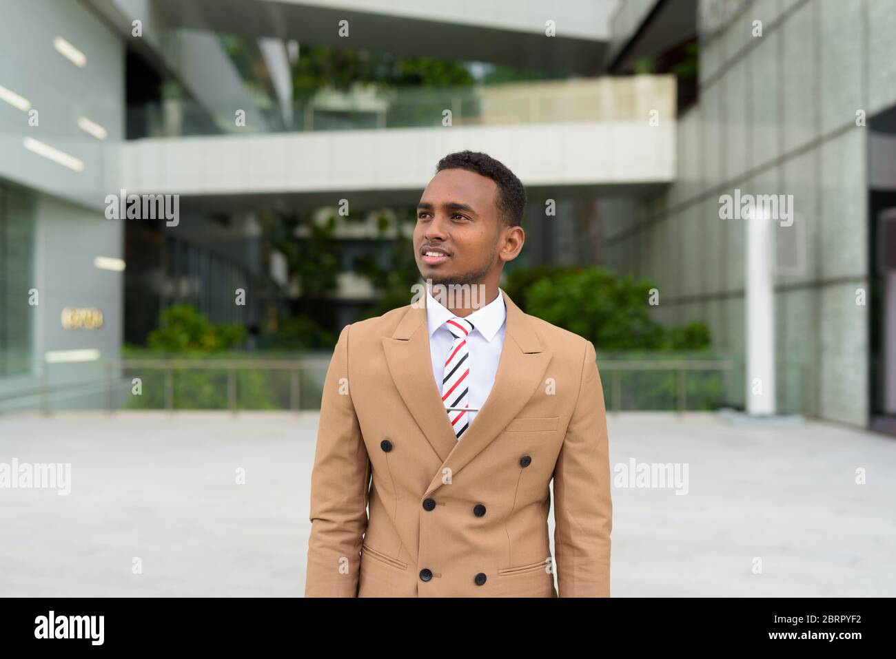 Felice giovane bell'uomo d'affari africano che pensa in città Foto Stock