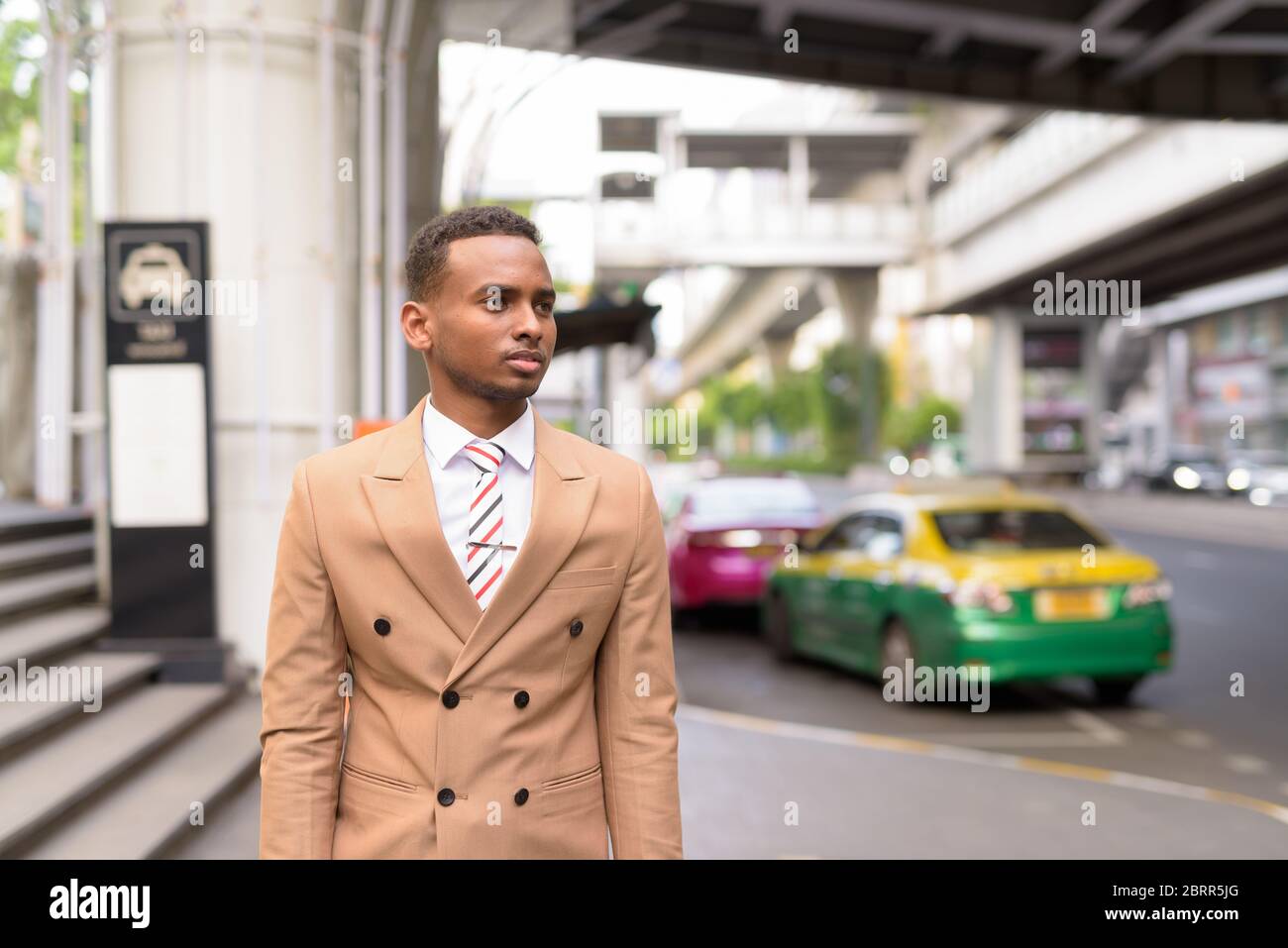 Giovane bell'uomo d'affari africano in attesa di un taxi in città Foto Stock