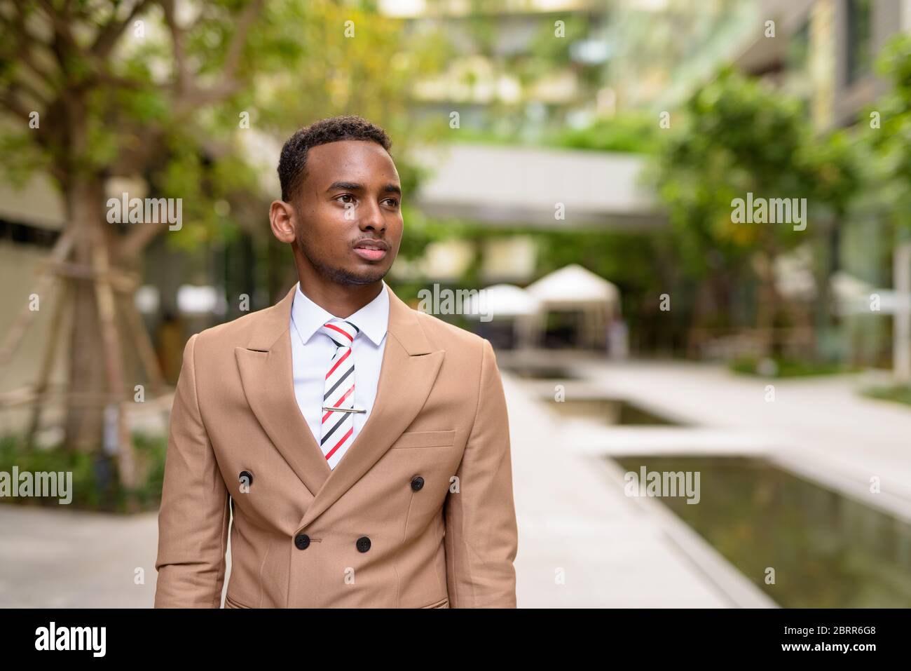 Giovane bell'uomo d'affari africano che pensa con la natura in città Foto Stock
