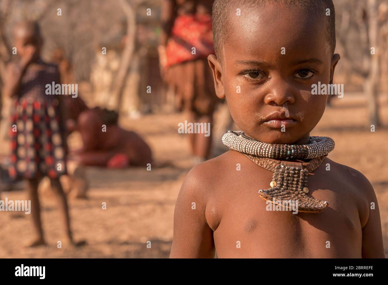 Namibia rurale - 21 agosto 2016. Un ragazzo giovane che indossa collane tribali in un remoto villaggio di Himba, ha un naso che cola da un freddo. Foto Stock