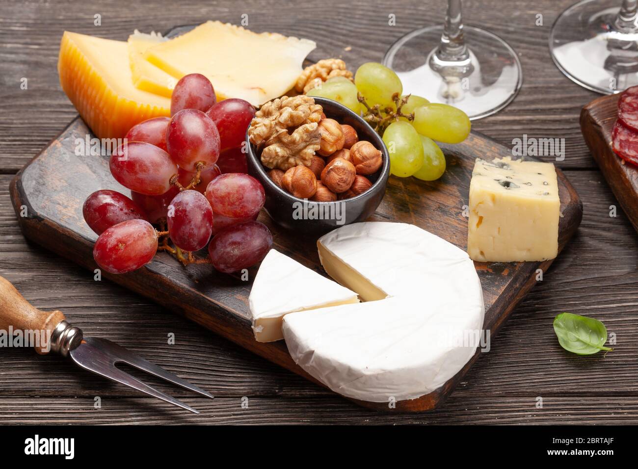 Antipasto di formaggi, uva e noci. Piatto di selezione degli antipasti e bicchieri con vino Foto Stock