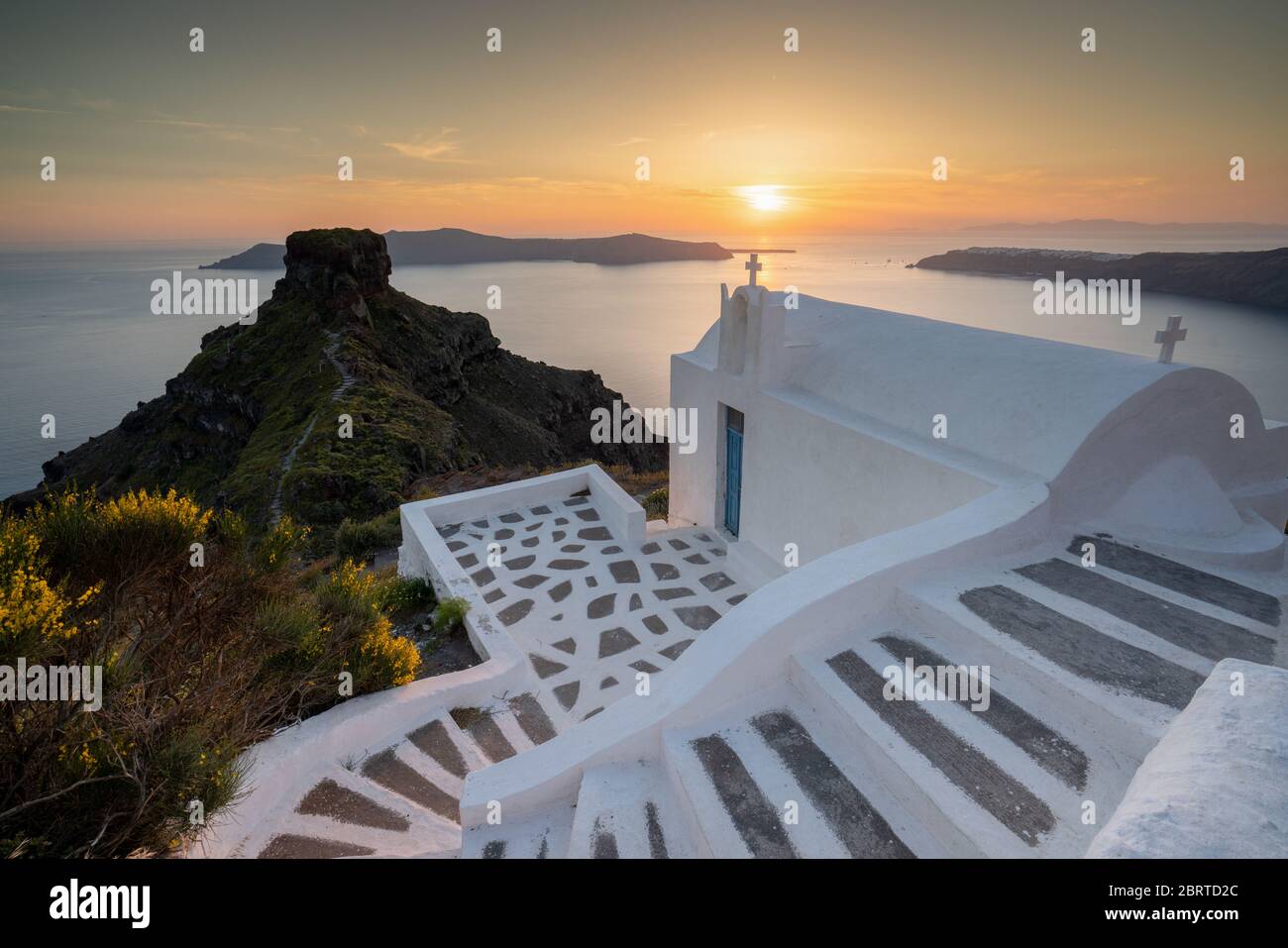 Santorini chiesa dipinta di bianco che si affaccia sulla Caldera e il mare al tramonto con linee guida e gradini Foto Stock