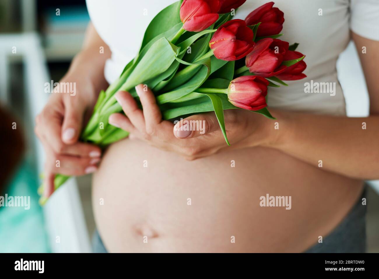 Primo piano di addome incinta umana e mazzo di fiori Foto Stock