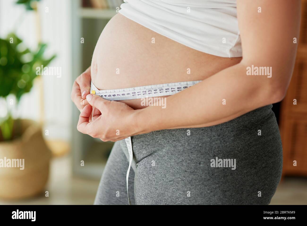 Donna incinta che usa il metro a nastro per controllare l'addome Foto Stock