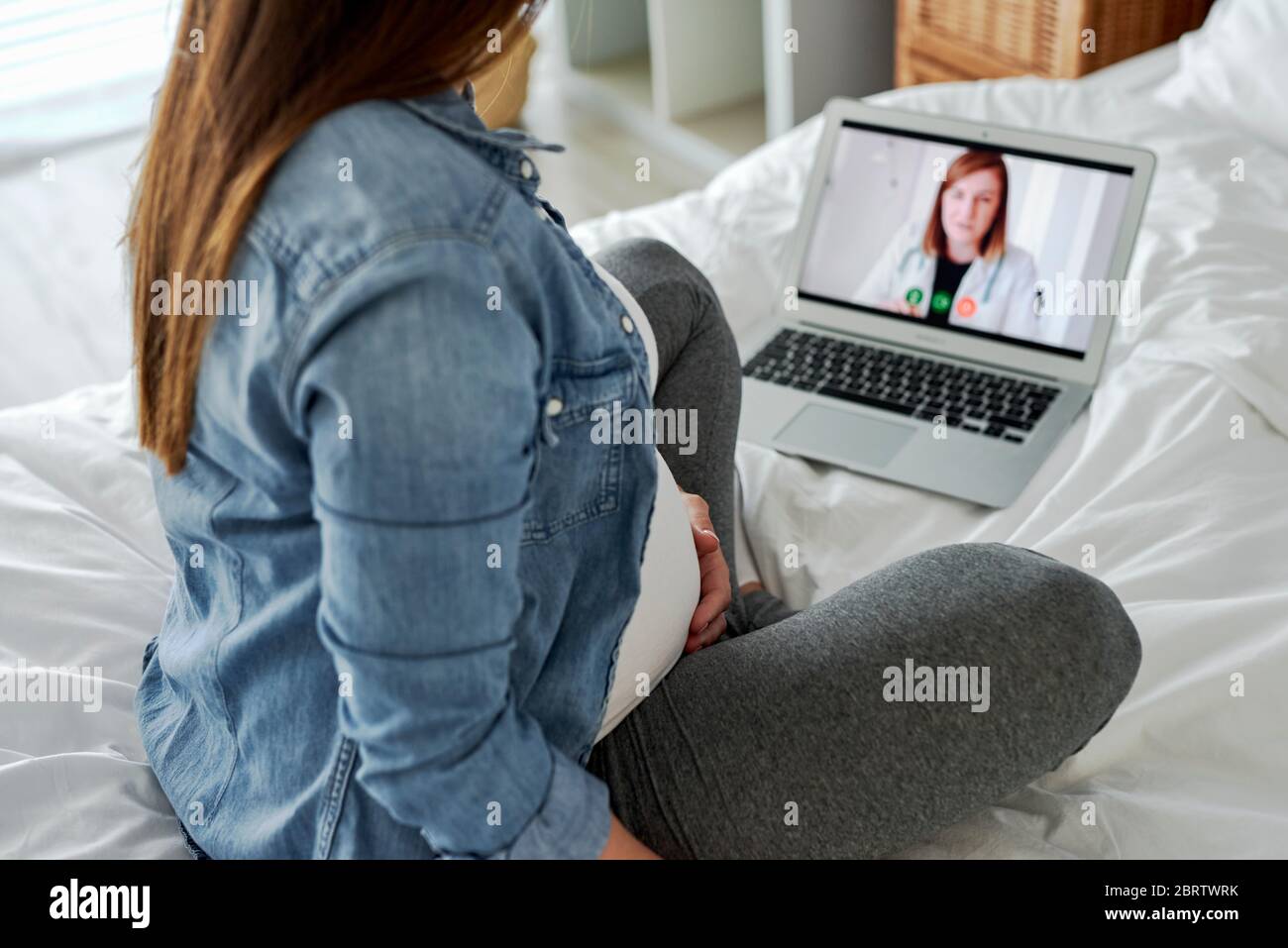 Donna in gravidanza avanzata con videoconferenza con medico Foto Stock