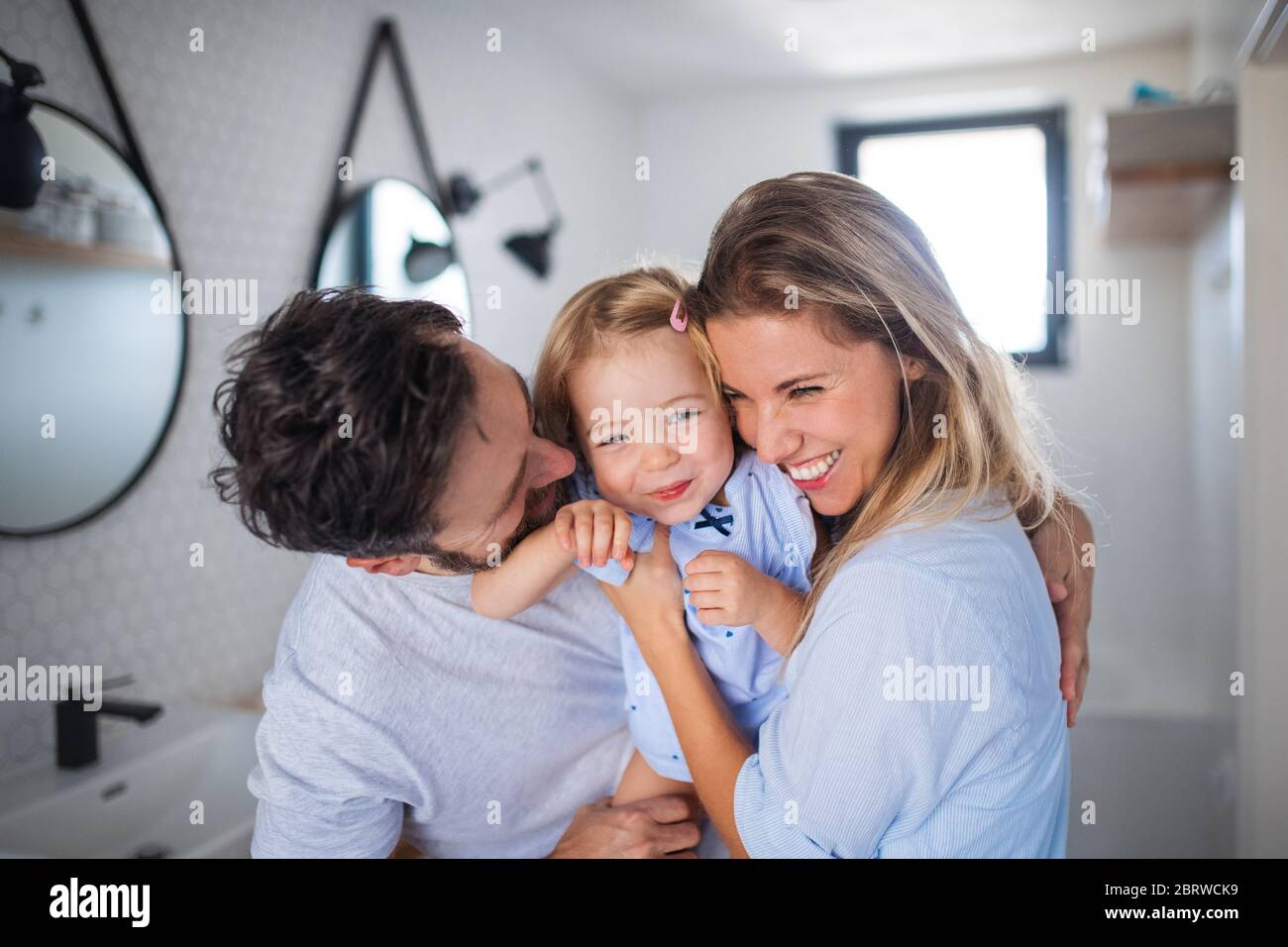 Giovane famiglia con piccola figlia al chiuso in bagno, abbracciando. Foto Stock