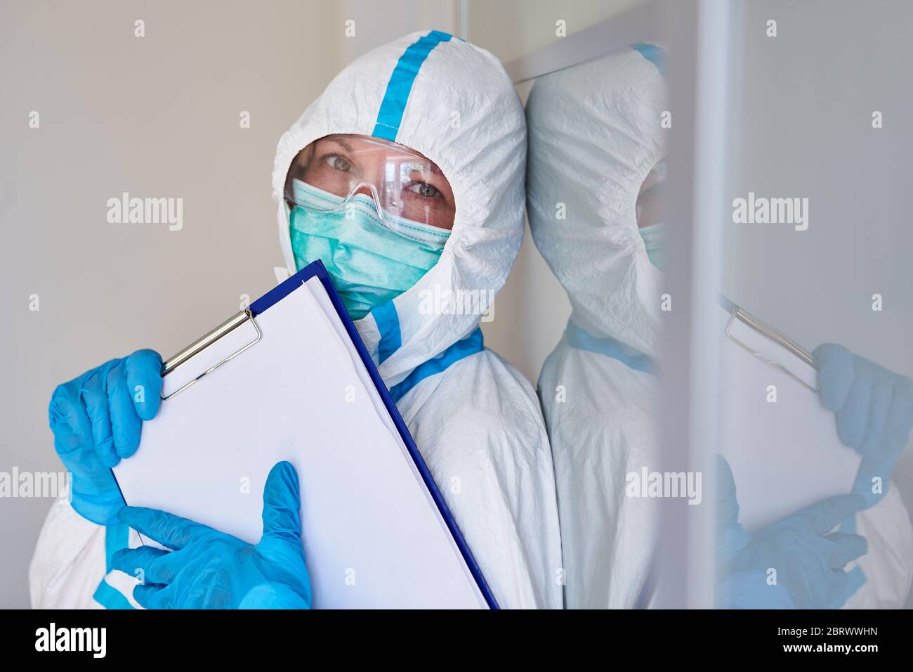 Scout di contenimento o personale infermieristico in abbigliamento protettivo con lista visitatori per il monitoraggio dei contatti a causa di pandemia di coronavirus Foto Stock