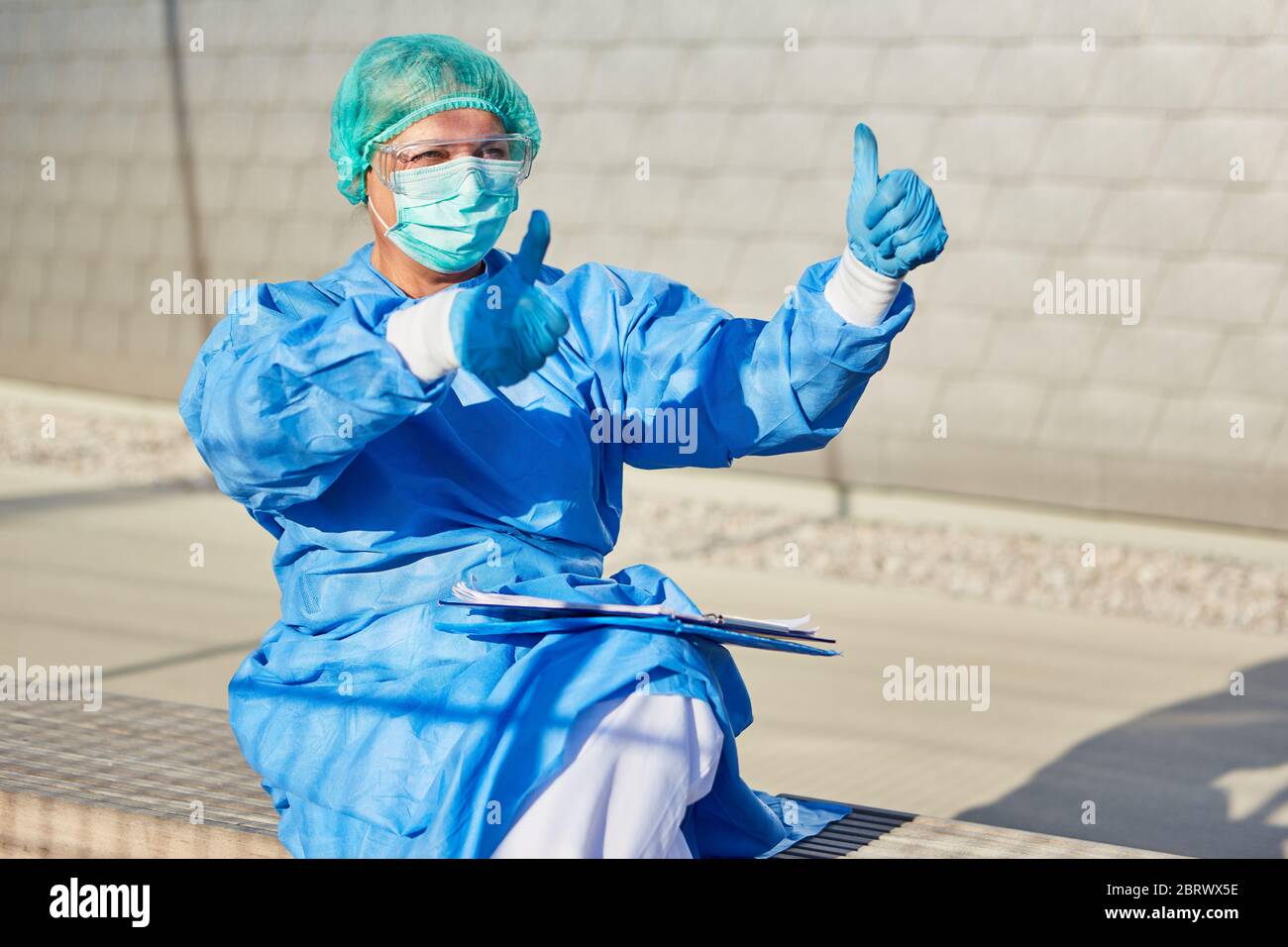 La scout medico o di contenimento negli indumenti protettivi mostra i pollici durante i controlli durante la pandemia del coronavirus Foto Stock