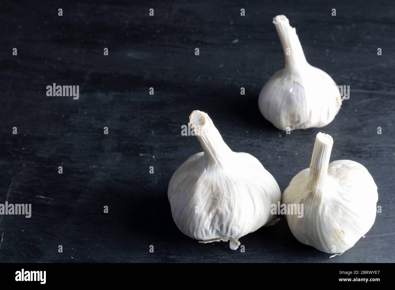 tre teste di aglio situate sul lato destro con fondo nero. cibo scuro Foto Stock