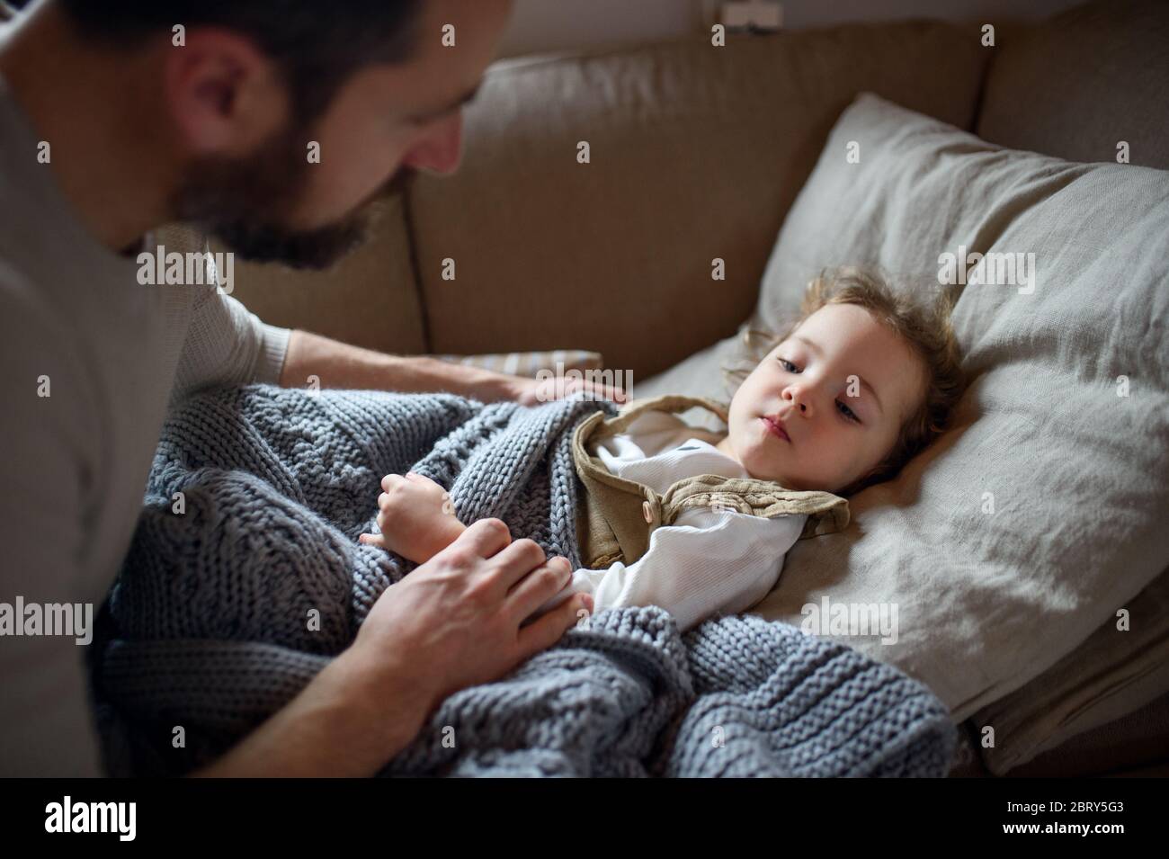 Padre che controlla la figlia piccola malata che si trova in letto all'interno della casa. Foto Stock