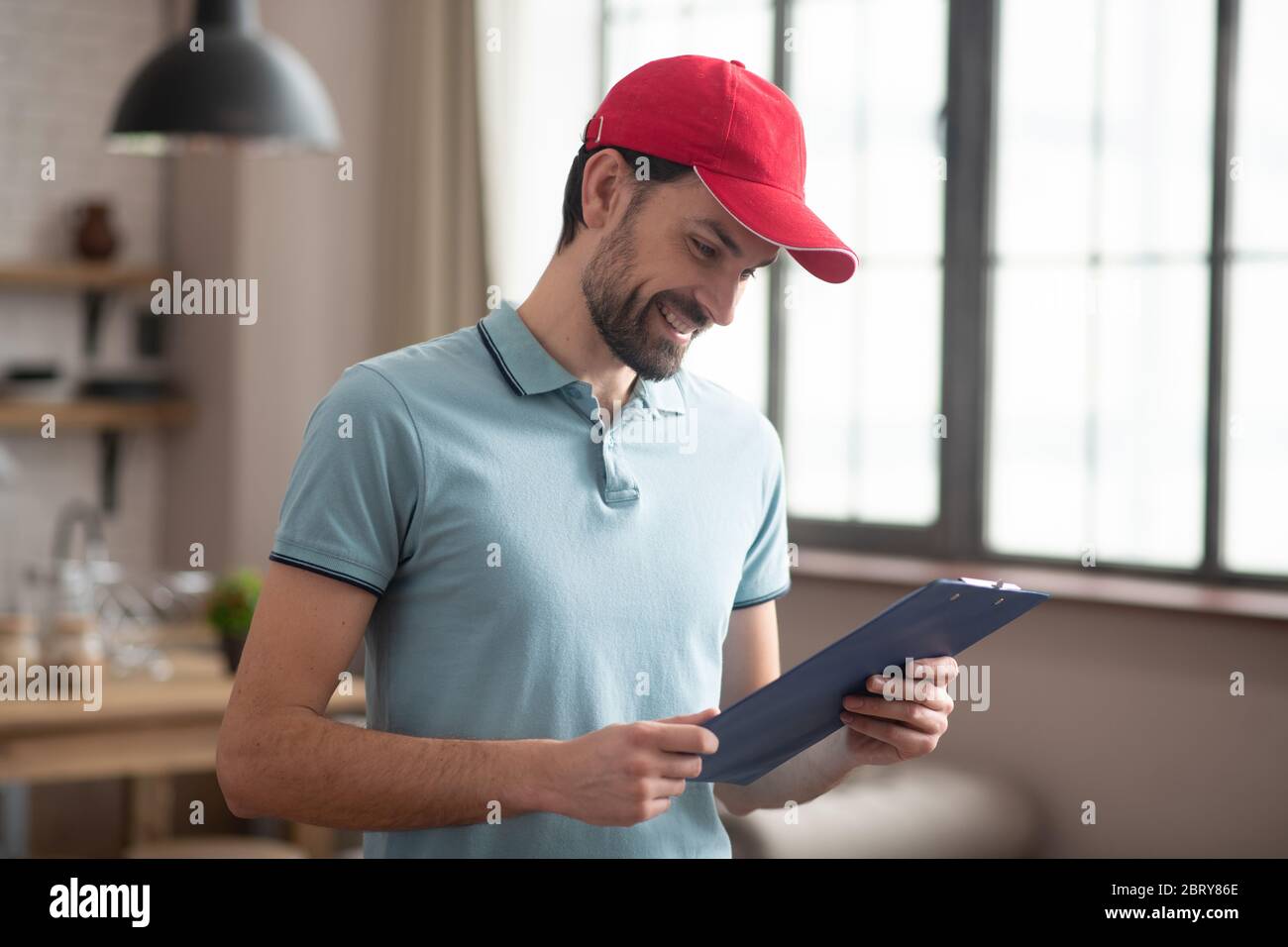 Persona di consegna in un cappello rosso guardando la lettera di vettura e sorridendo Foto Stock