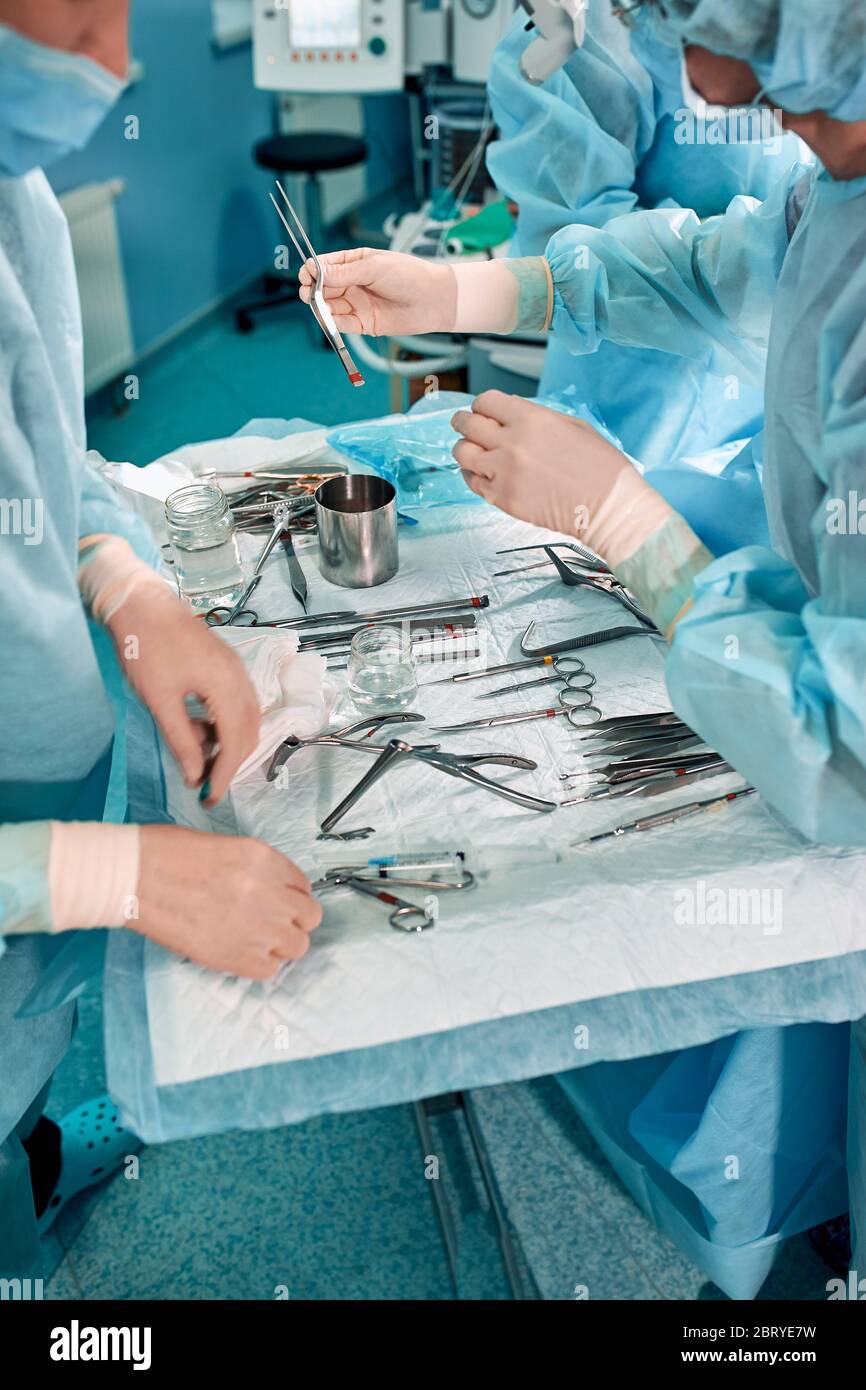 Strumenti sterili sul tavolo operatorio, un team di medici definisce gli strumenti per l'operazione. Molte mani vengono fermentate in guanti sterili. Foto Stock