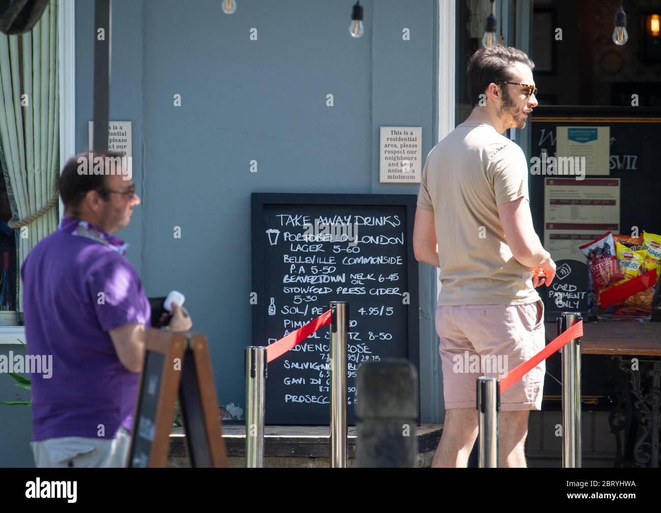 I clienti osservano le distanze sociali mentre si accodano per le bevande da asporto fuori dal pub Althorp, a Wandsworth, Londra, dopo l'introduzione di misure per portare il paese fuori dai blocchi. Foto Stock