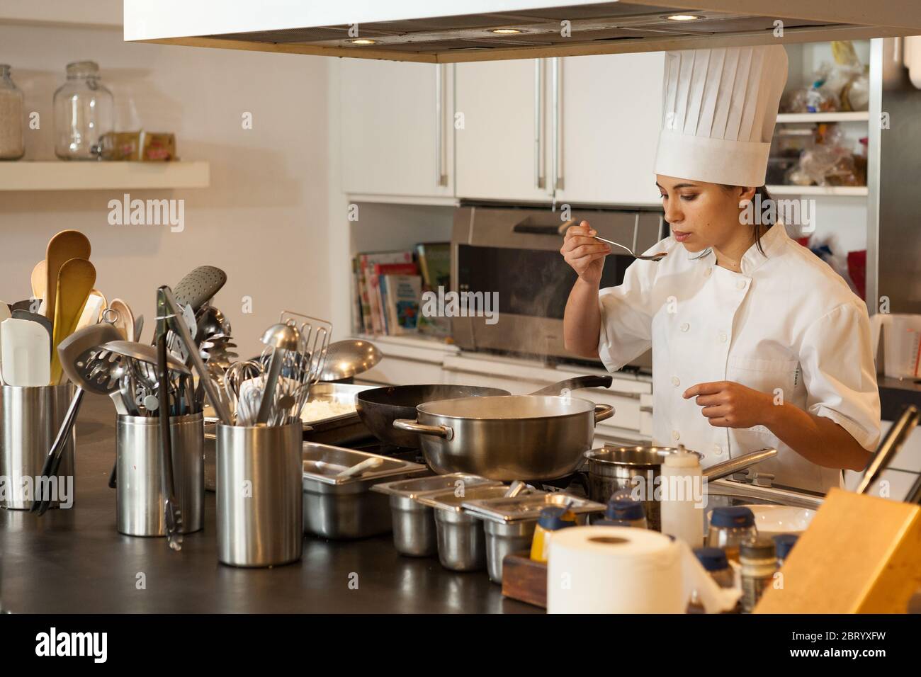 Chef femminile che indossa cappello dello chef in piedi in stufa in cucina, degustazione di cibo. Foto Stock