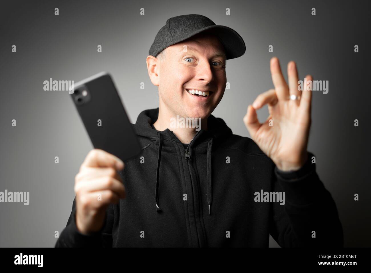 Uomo in abiti neri felice con il messaggio sul telefono o il telefono stesso. Foto Stock