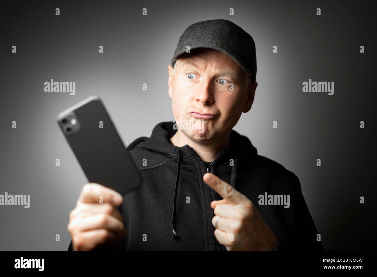 Uomo in abiti neri che indica il messaggio sul telefono o il telefono stesso Foto Stock