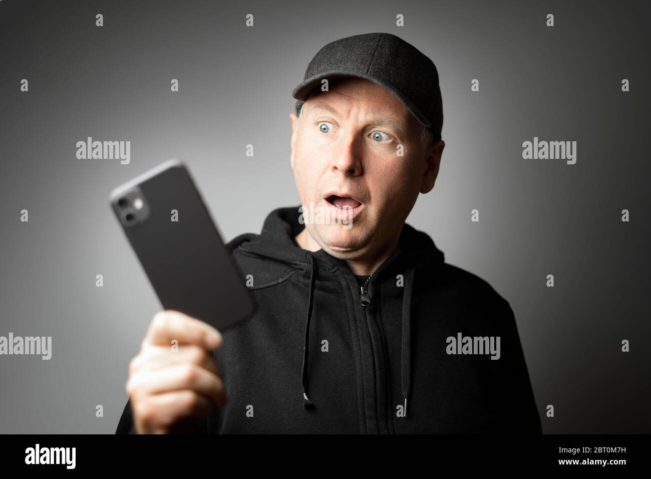 Uomo in abiti neri scioccato con il messaggio sul telefono o telefono stesso Foto Stock