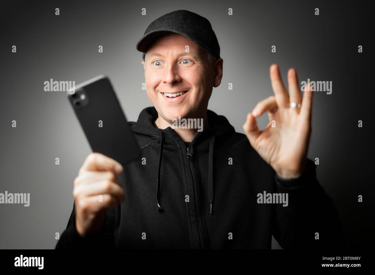 Uomo in abiti neri felice con il messaggio sul telefono o il telefono stesso. Foto Stock