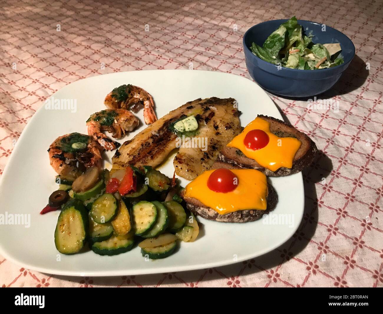 Filetto di cichlid alla griglia con burro di erbe, gamberi, verdure mediterranee e pane all'aglio gratinato e insalata a parte Foto Stock