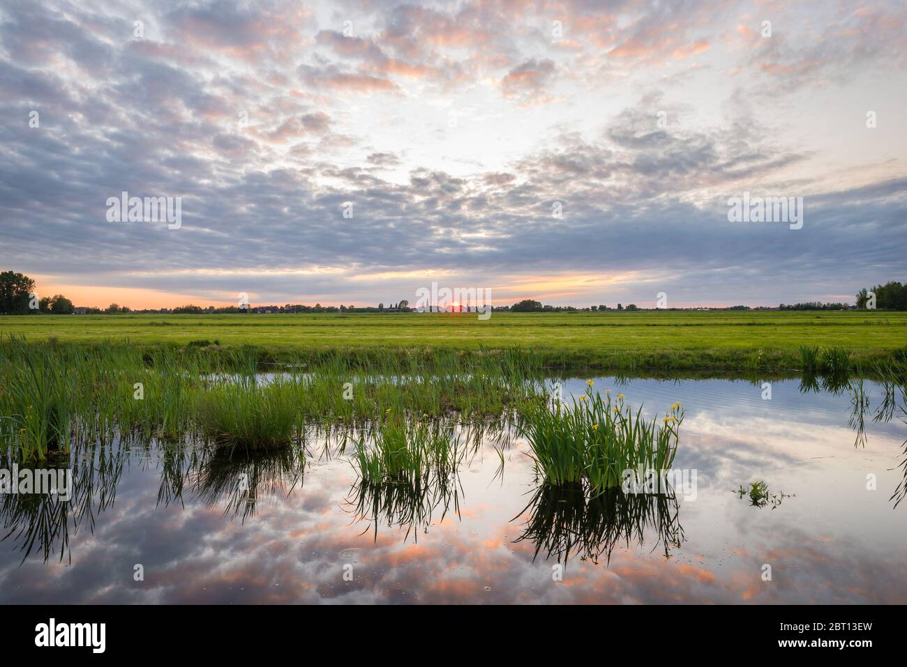 Il sole si stagna su una zona umida in Olanda. Le nuvole sono illuminate dall'ultima luce del sole e splendidamente illuminate in acqua. Foto Stock