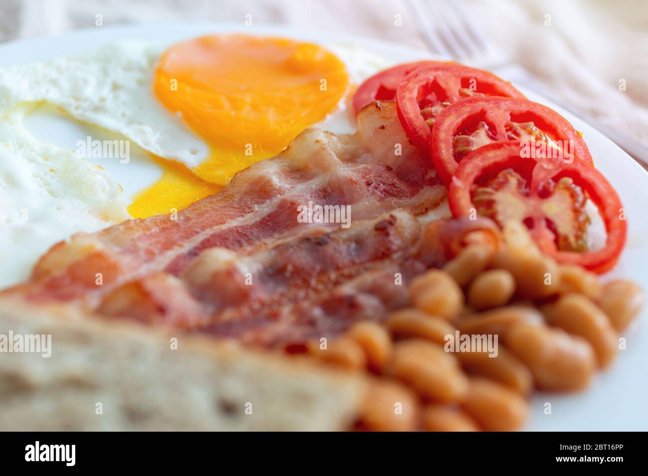 Primo piano della colazione inglese tradizionale: Uova fritte, pancetta, fagioli, pane tostato e pomodoro su un piatto. Foto Stock