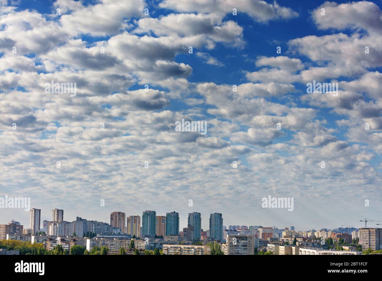 I raggi del sole illuminano brillantemente le nuvole grigio-bianco nel cielo blu sopra la città risvegliante. Luce brillante nel cielo nuvoloso del mattino. Foto Stock