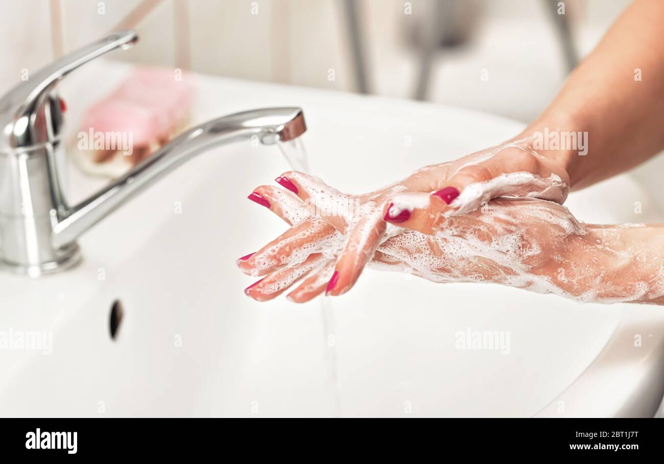 Giovane donna che le lava le mani sotto rubinetto d'acqua con sapone. Dettagli sulla pelle ricoperta di suds. Concetto di igiene personale - coronavirus covid 19 focolaio Foto Stock