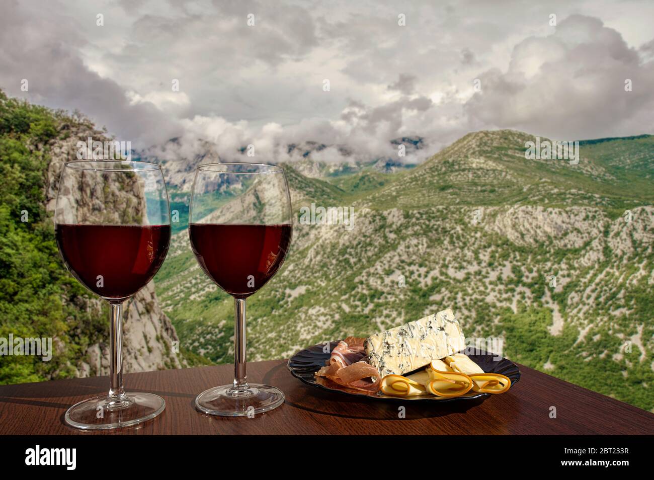Due bicchieri di vino con assortimento di salumi sulla vista delle montagne con le nuvole in Croazia. Cena in un bar o ristorante con vista sulle montagne. Foto Stock