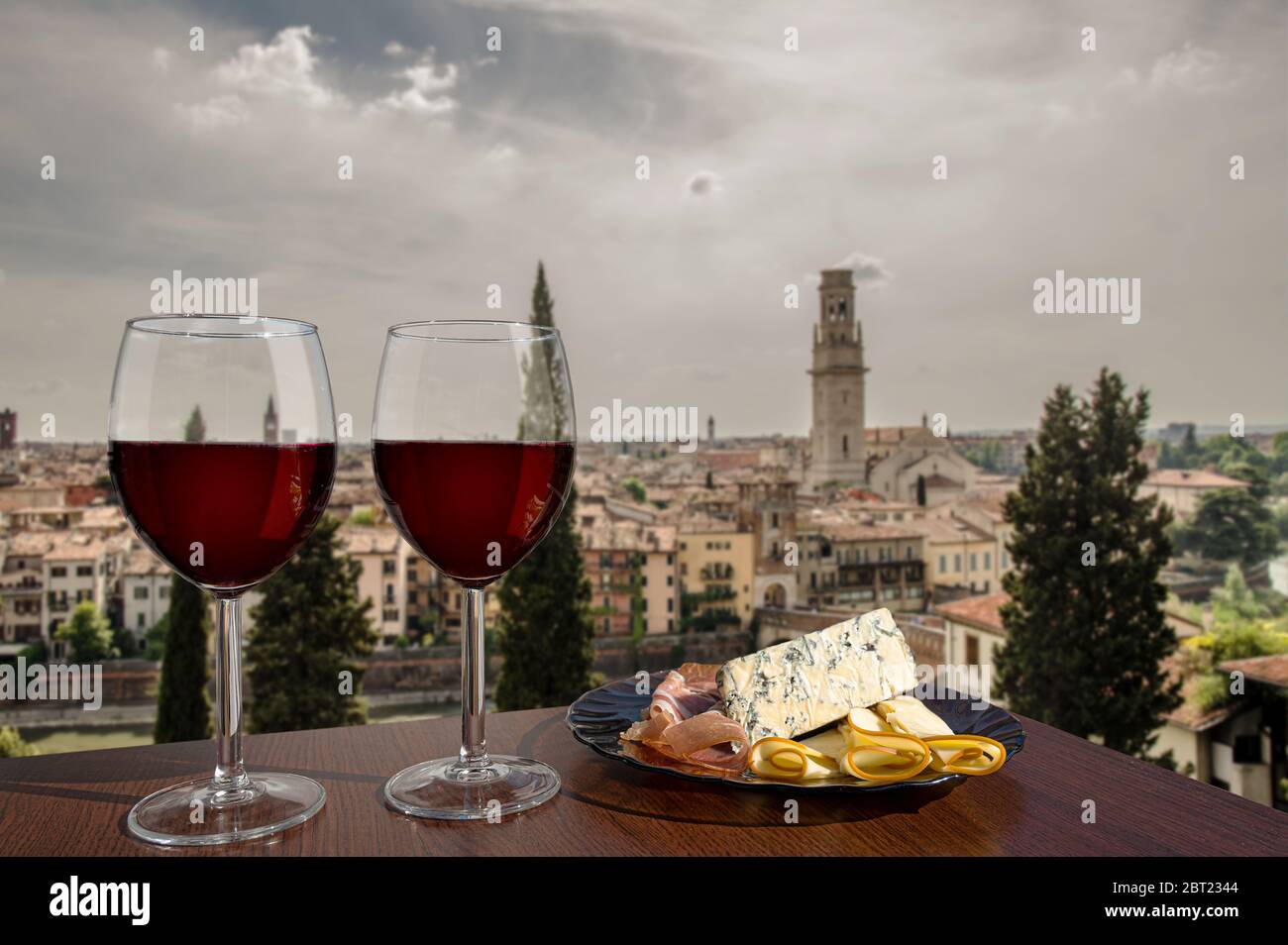 Due bicchieri di vino con assortimento di salumi con vista su Verona. Bicchiere di vino rosso con diversi spuntini - piatto con prosciutto, affettato, formaggio Foto Stock