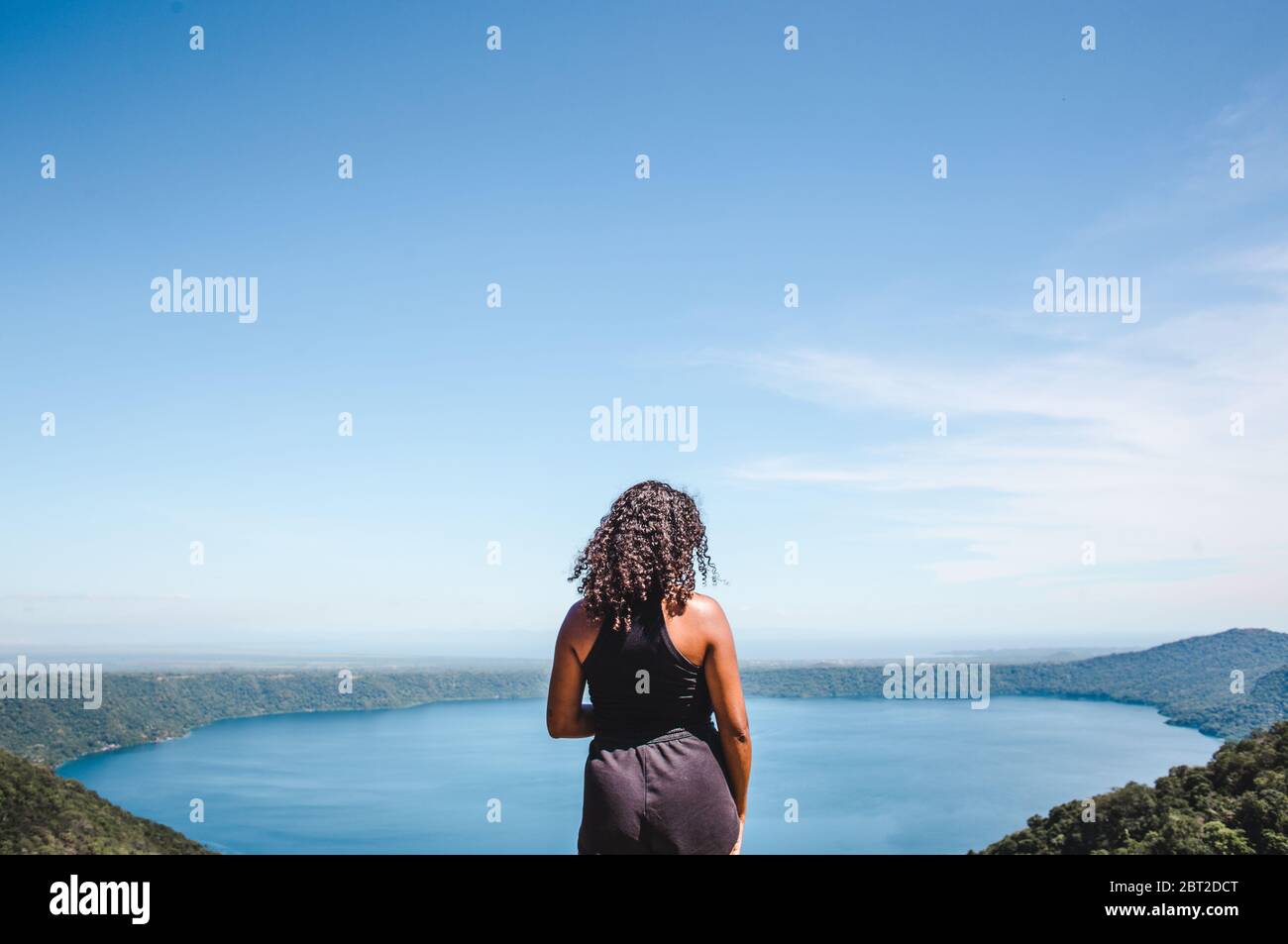 La ragazza millenaria di zaino in spalla di razza mista guarda fuori dal punto di vista aereo sopra Laguna de Apoyo, un lago craterico vicino Masaya, Nicaragua Foto Stock