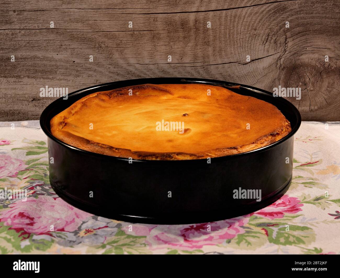 La cheesecake della nonna, appena sfornata, ancora in teglia, su un tovaglia, su sfondo di legno. Foto Stock