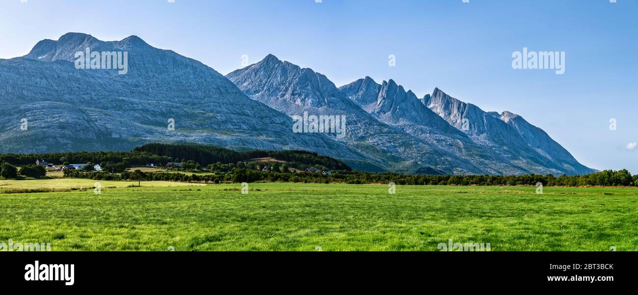 Vista panoramica su cinque delle montagne Seven Sisters di Sandnessjoen, idealmente verde erba, piccolo villaggio norvegese e montagne accanto al campo. S Foto Stock