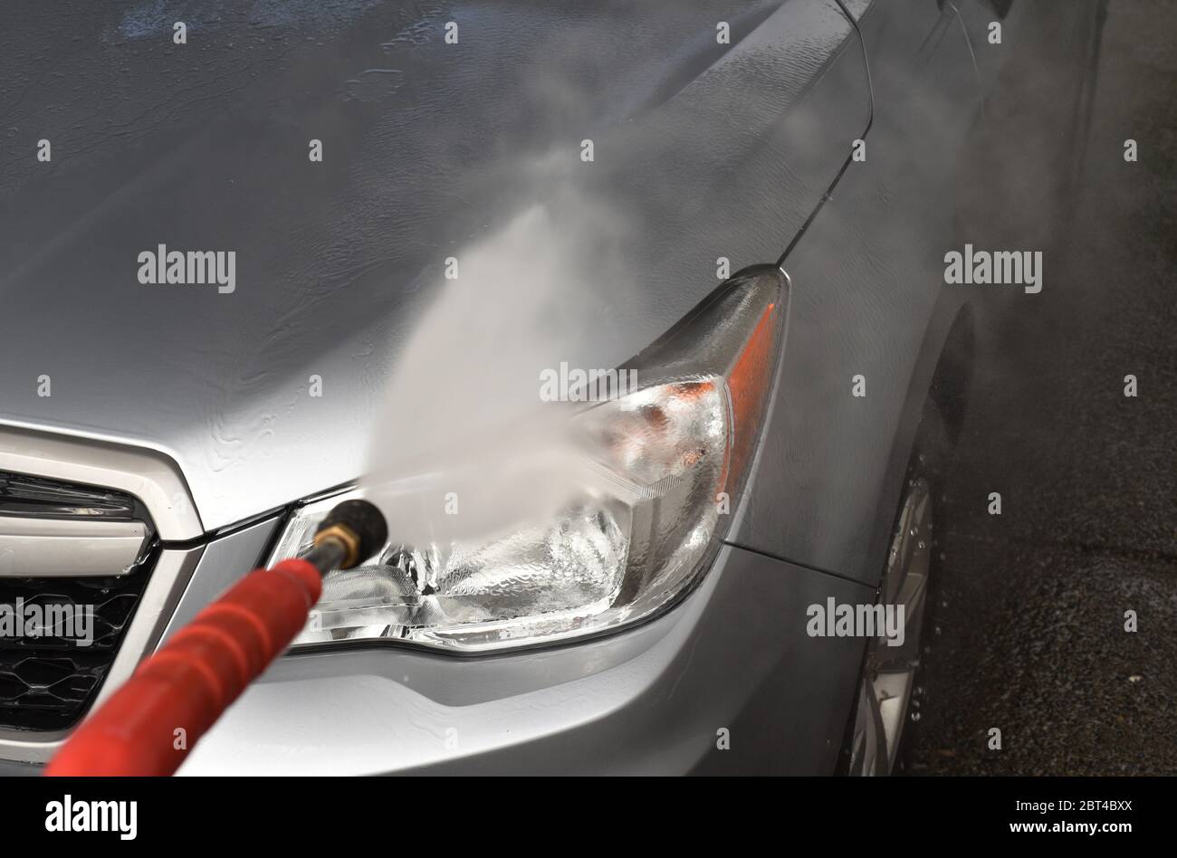 Sciacquare il cofano anteriore e la luce della testa su un'auto color grigio argento 2016 Subaru Forester SUV con una lancia a DIY (fai da te) autolavaggio Foto Stock