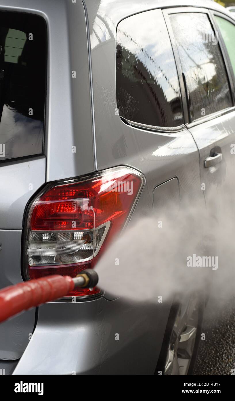 Sciacquare la luce posteriore su un'auto SUV color grigio argento 2016 Subaru Forester con una lancia a spruzzo a DIY (fai da te) autolavaggio Foto Stock