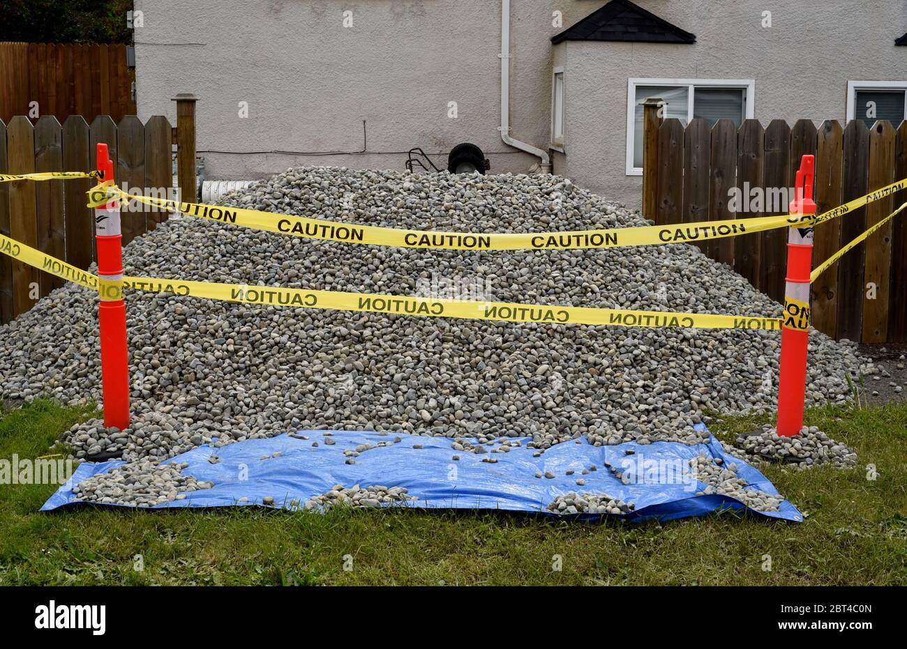 Il nastro di attenzione circonda un mucchio di ghiaia che si situa su un tarp blu davanti ad una casa e ad un cortile suburbani. Le pietre piccole possono essere usate per riempimento, drenaggio Foto Stock