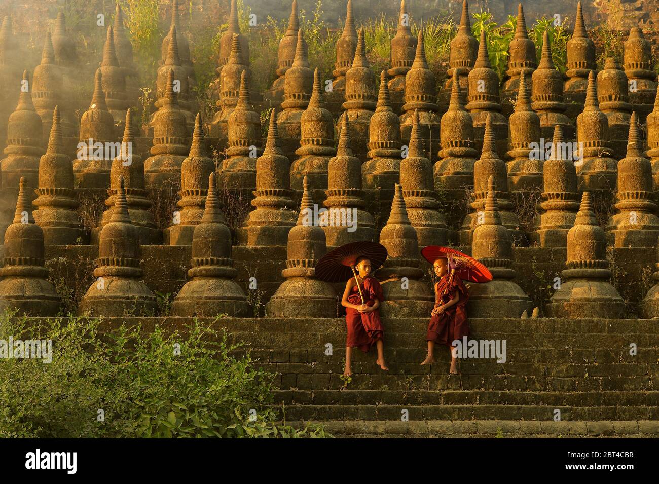 Due monaci novizi seduti, su un muro, Mrauk-U, Myanmar Foto Stock
