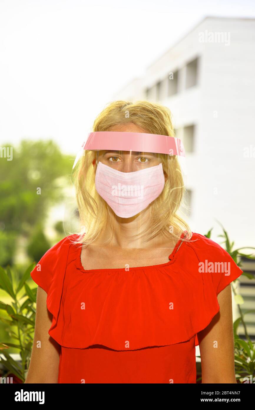 Donna con maschera chirurgica rosa e visiera protettiva sul viso, su sfondo urbano. Concetto di epidemia COVID-19, quarantena per il pubblico Foto Stock