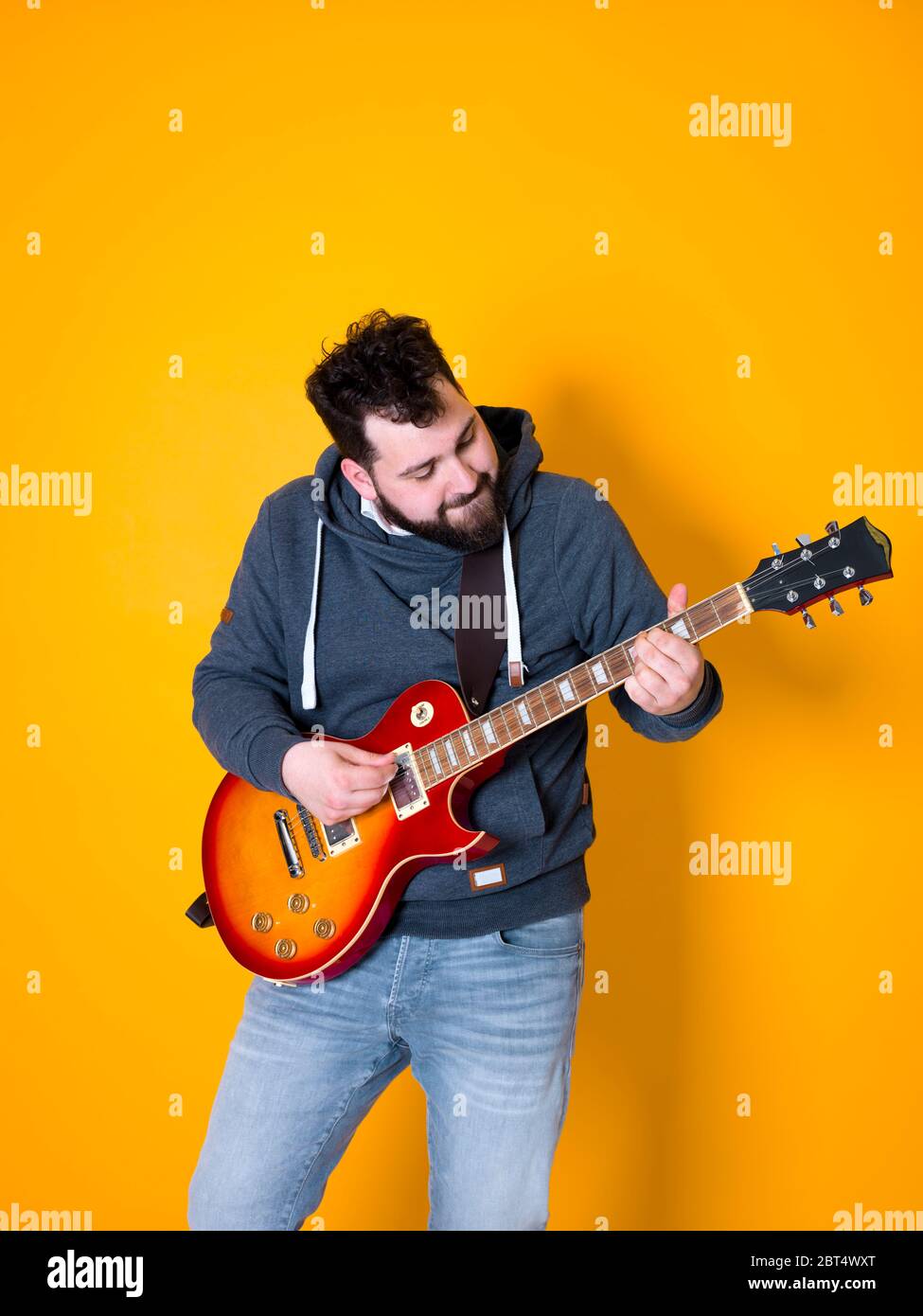 L'uomo con i capelli neri e barba suonare la chitarra elettrica di fronte a uno sfondo giallo Foto Stock