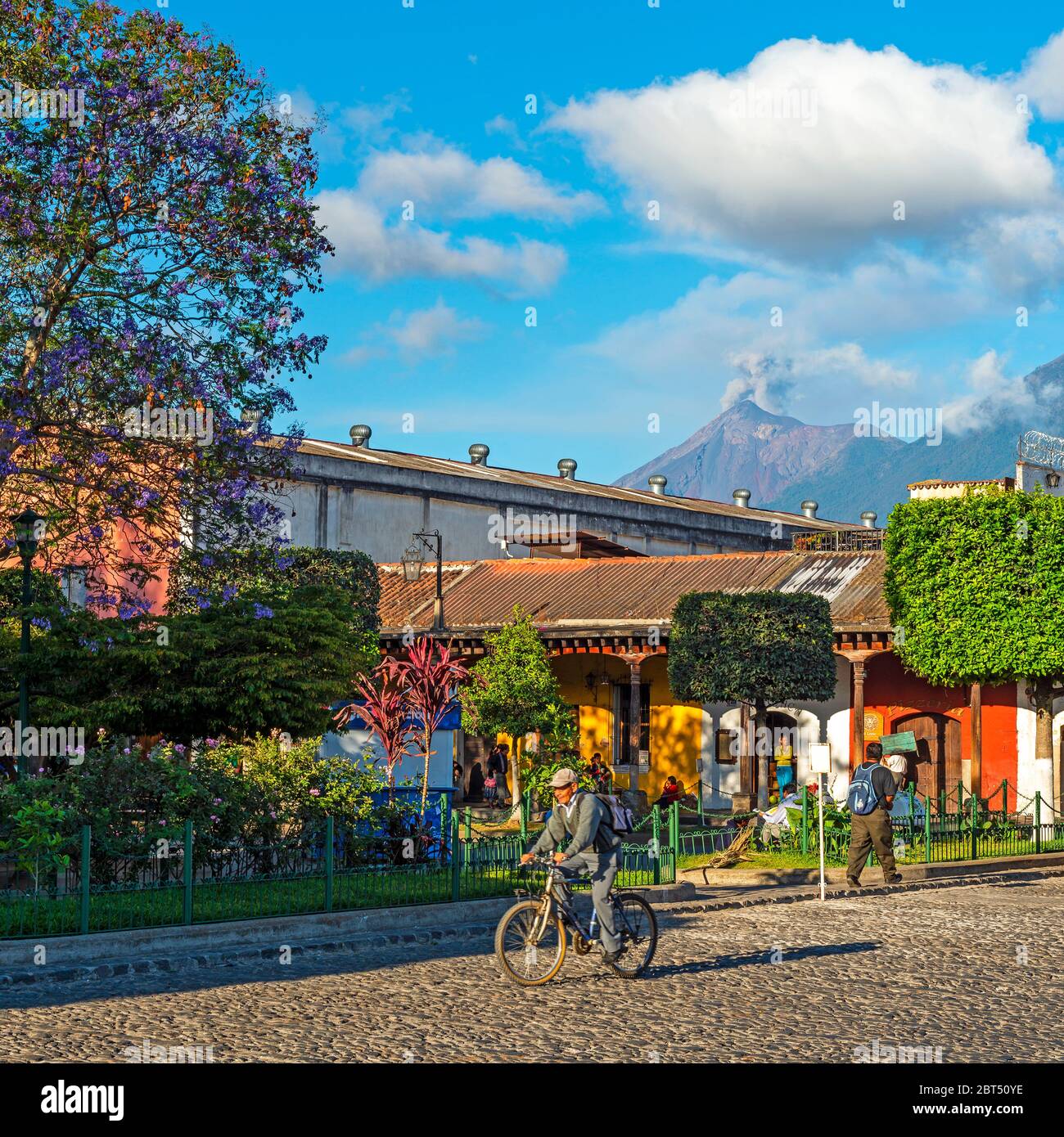 Vita cittadina ad Antigua con un uomo anziano che cavalcano una bicicletta durante un'esplosione di ceneri vulcaniche e un'eruzione del vulcano Fuego, Guatemala. Foto Stock