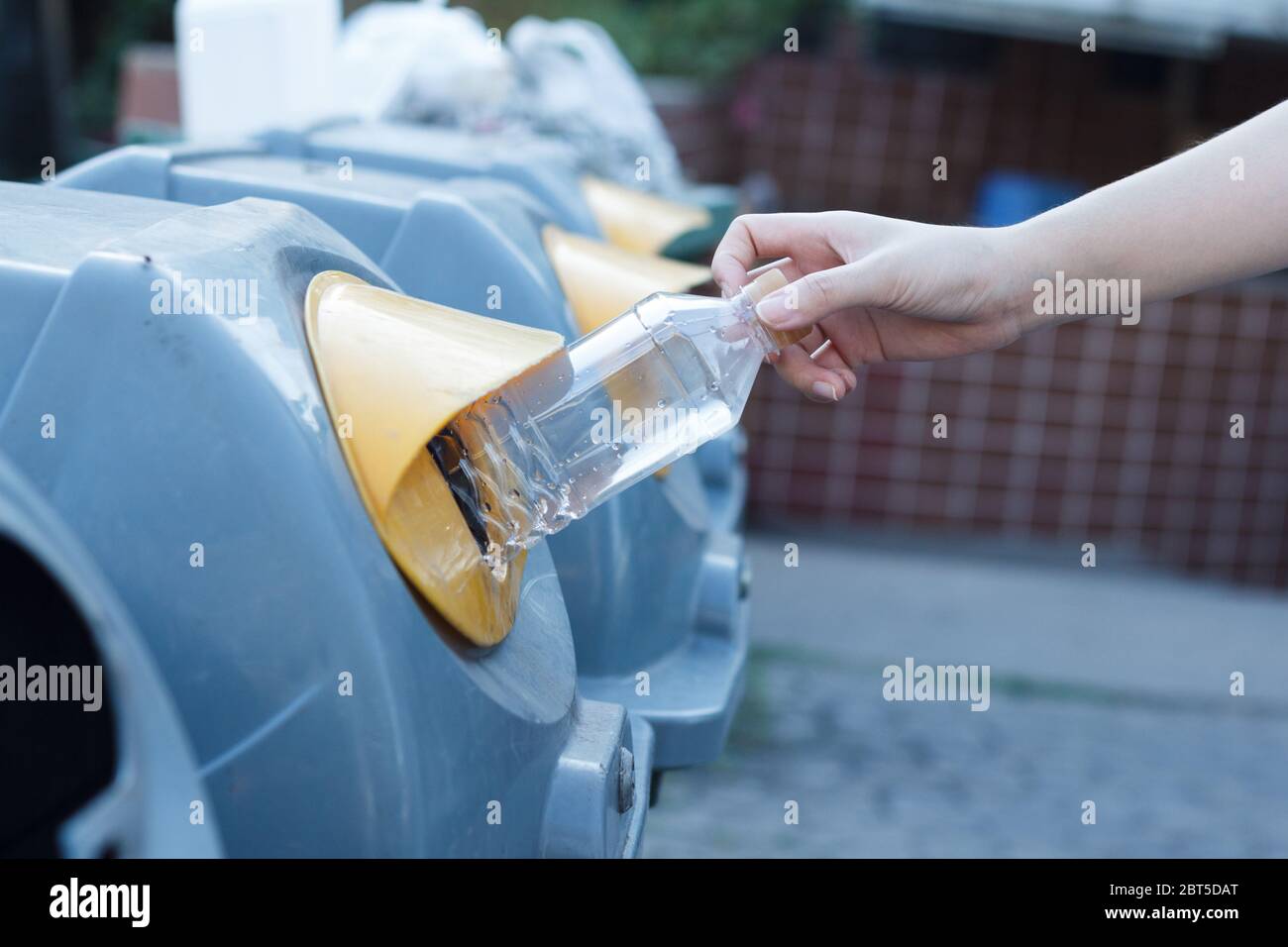 Closeup donna mano gettando bottiglia vuota di plastica in contenitore di riciclaggio. Isolato esterno sfondo. Foto Stock